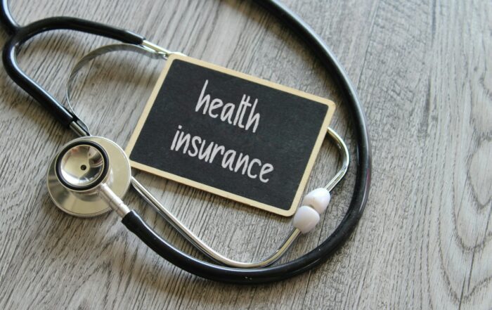 Stethoscope and chalkboard with text HEALTH INSURANCE on wooden table
